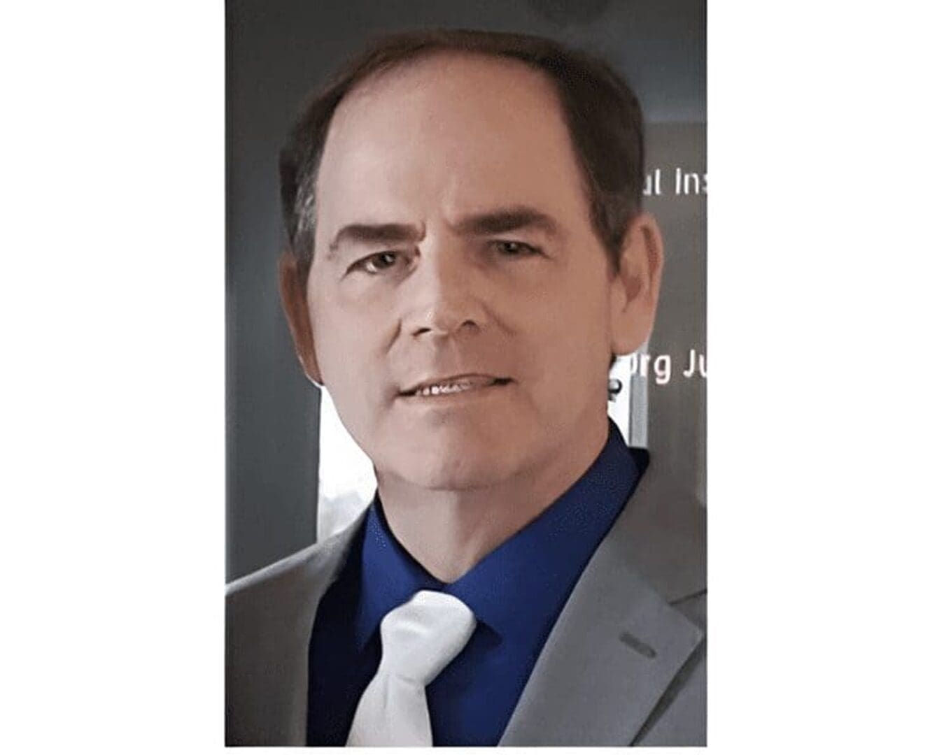 Man in suit with blue shirt, smiling.